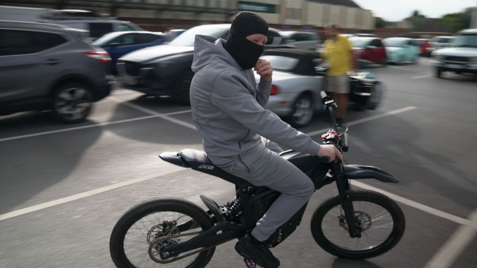 Man wearing balaclava and tracksuit on electric motorbike