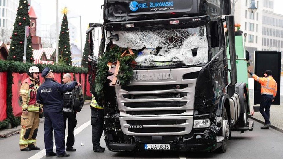 A policeman and firemen stand next to a truck on 20 December 2016 at the scene where it crashed into a Christmas market near the Kaiser-Wilhelm-Gedaechtniskirche (Kaiser Wilhelm Memorial Church) in Berlin