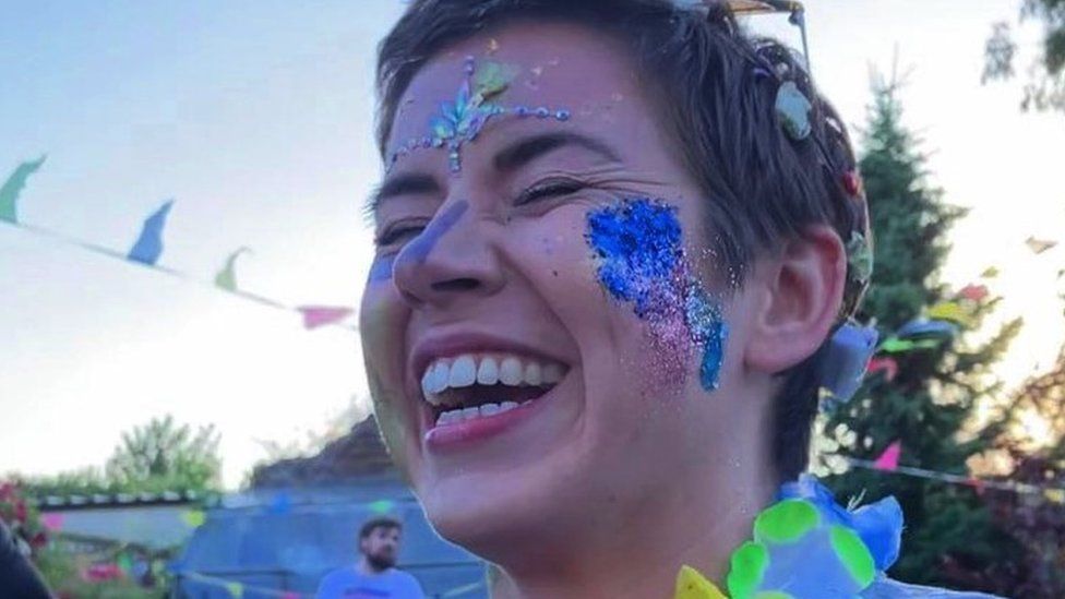 Danielle Moore. Her eyes are closed and she is laughing. She is wearing face paint and glitter on her forehead and cheeks.