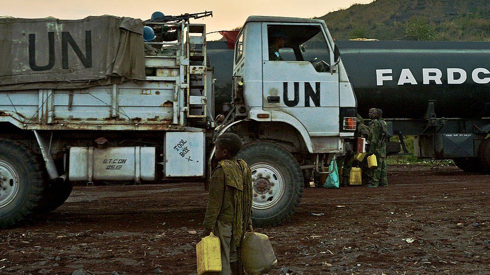 UN lorry goes past boy holding jerry cans on side of the road in Congo
