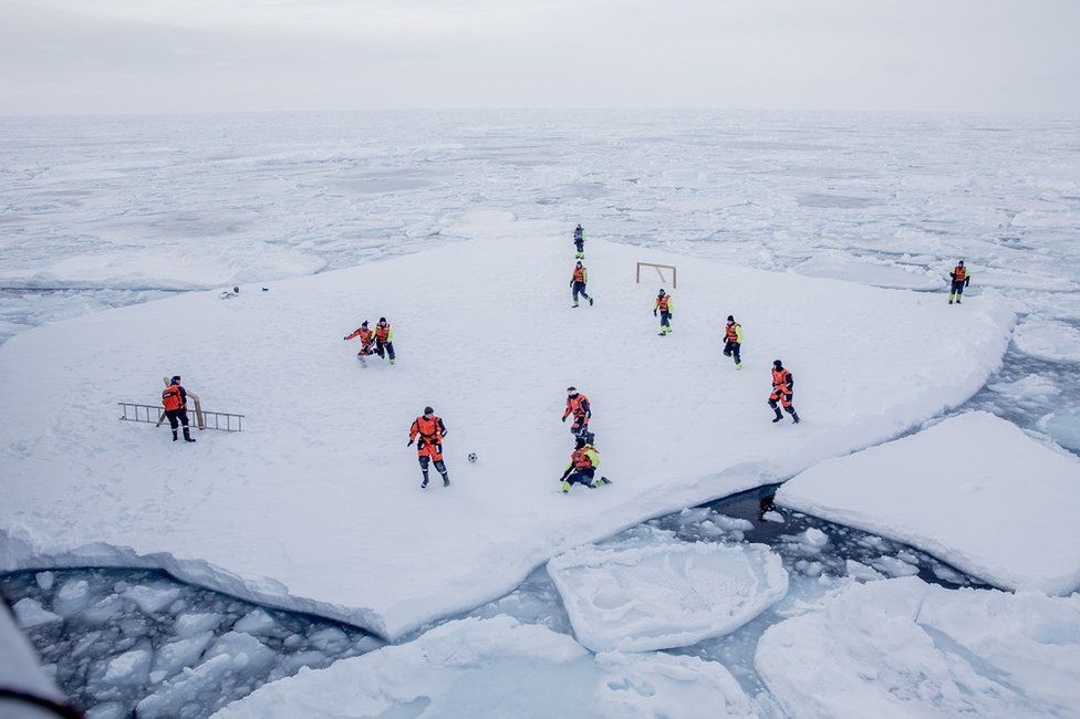 Norveç devriye gemisi KV Svalbard'ın tayfası Grönland yakınlarında Mart ayında buz tutmuş denizin üstünde futbol oynuyor. Futbolcuların güvenliği için iki silahlı tayfa, arkadaşları futbol oynarken kutup ayılarına karşı nöbet tutuyor.