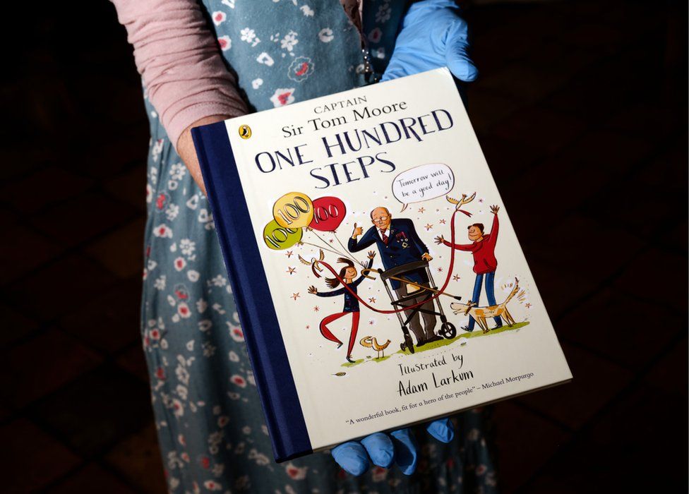 Captain Sir Tom Moore One Hundred Steps book for children held by a curator wearing blue nitrile loves