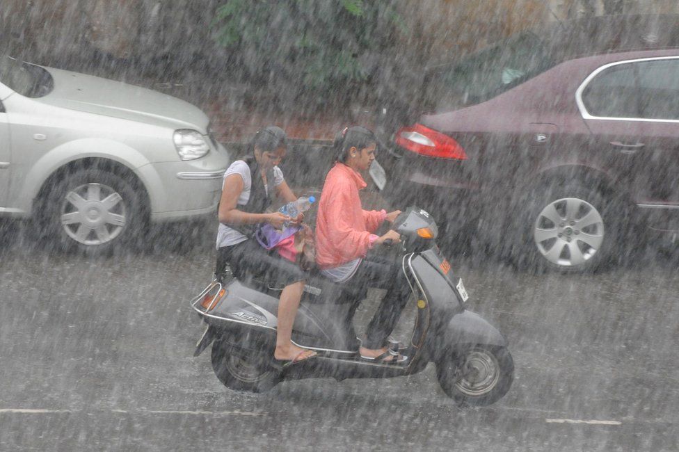 Indian women commute on a two wheeler during a heavy down pour of rain in Hyderabad on July 28, 2010.