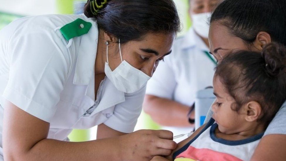 A nurse in Samoa gives a vaccine to a young girl
