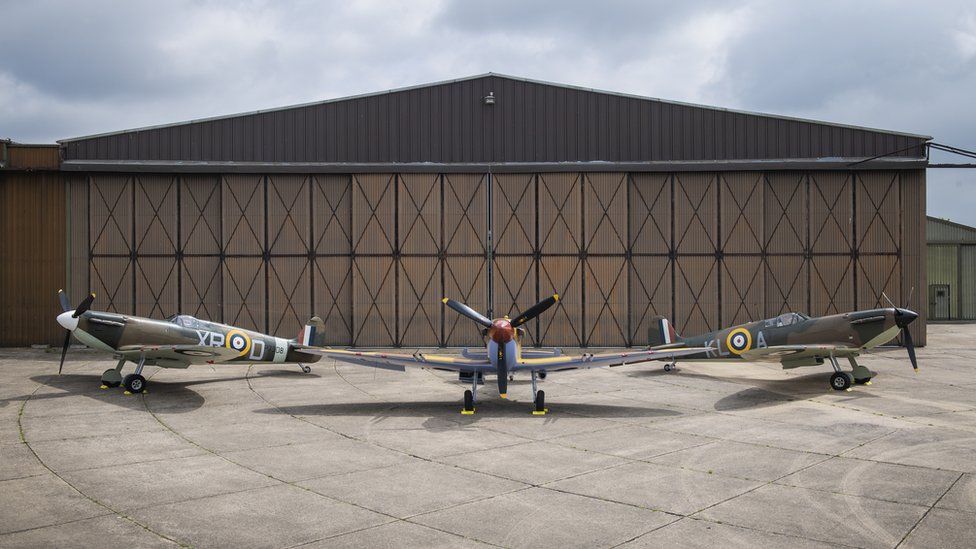 Three Spitfires (l-r Mk Ia X4650, Mk V JG891, Mk Ia R213) in front of a hangar at IWM Duxford