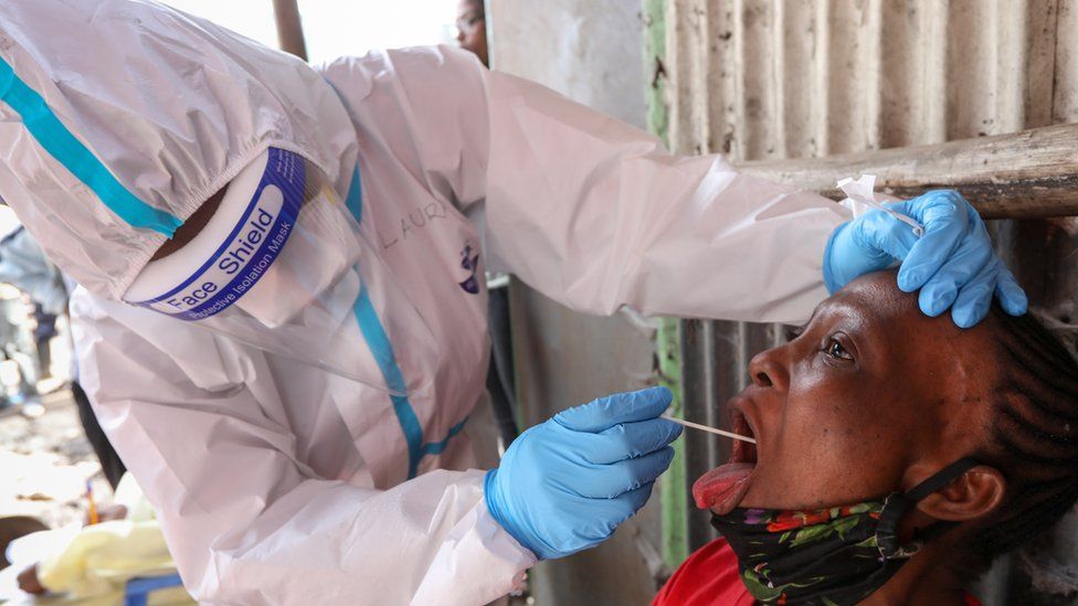 A Kenyan health worker in protective gear (L), uses a oral swab to collect a sample from a woman during a mass testing exercise for SARS-CoV-2 coronavirus