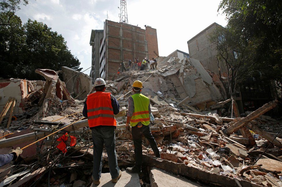 Rescue workers look at fellow workers searching for people under the rubble of a collapsed building