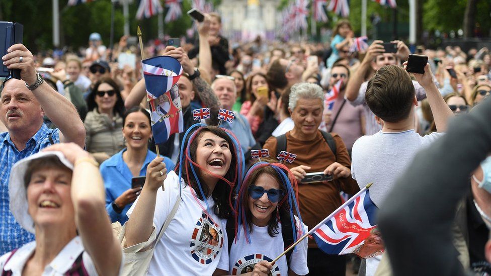Two women with blue and red hair extensions and Jubilee t-shirts wave union flags on a packed Mall outside Buckingham Palace