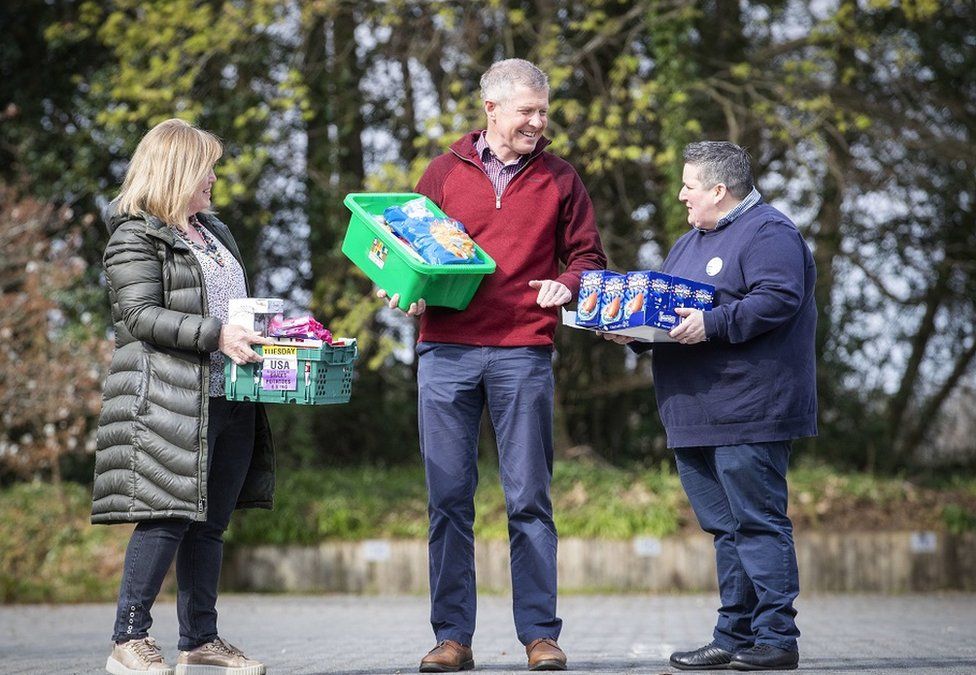 Scottish Liberal Democrat Leader Willie Rennie holds basket of food while speaking to two people