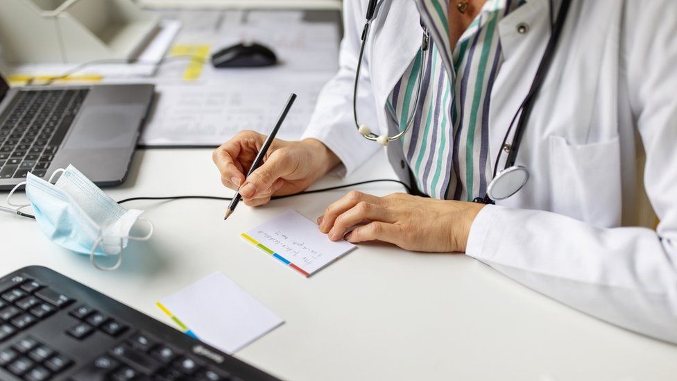 Close-up of a doctor preparing prescription while consulting a patient over video conference.