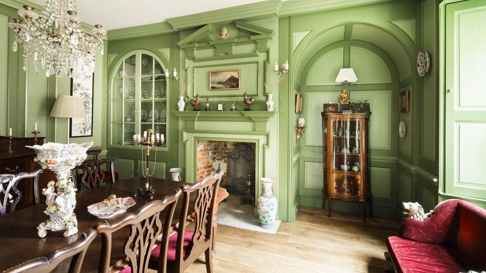 The manor house dining room. It has green walks, some of which is panelled and an open fireplace.