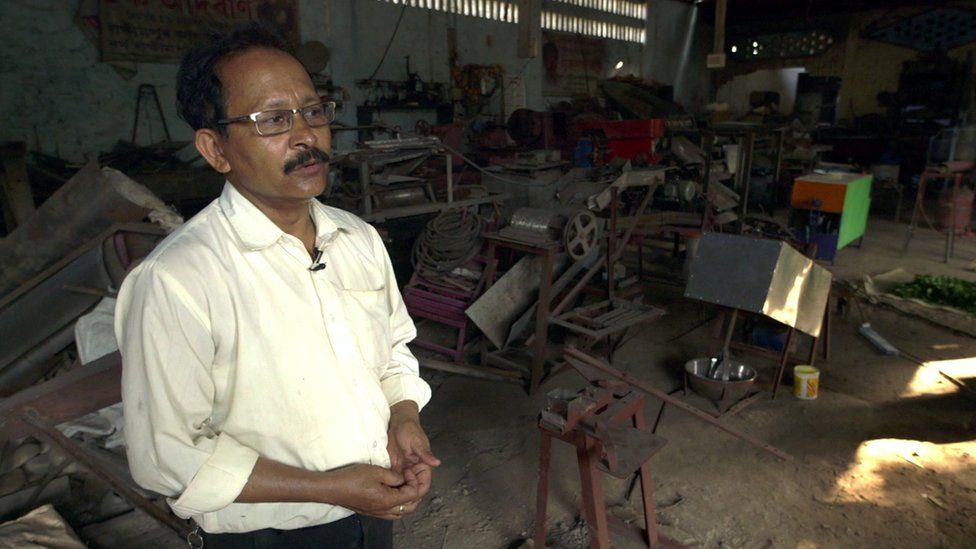 Uddhab in his workshop with lots of inventions and material and pieces behind him