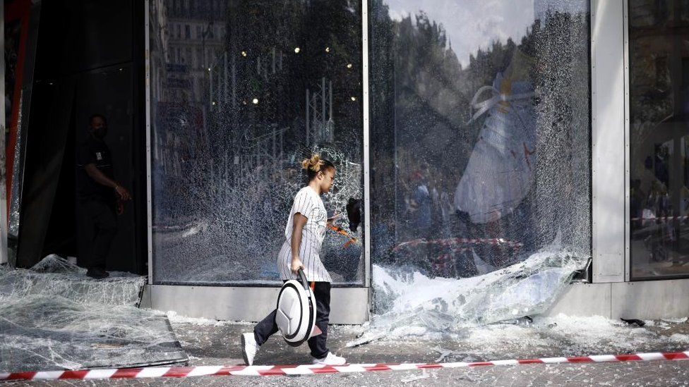 A woman walks past a broken Nike store front window following riots in Paris, France, 30 June 2023. Violence broke out all over France after police fatally shot Nael, a 17-year-old, during a traffic stop in Nanterre on 27 June