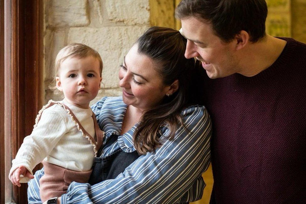 Holly (centre) pictured with her partner and baby