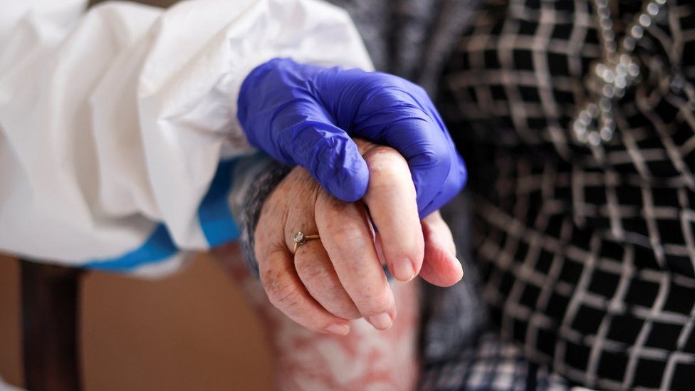 A care home resident's hand being held by someone wearing PPE