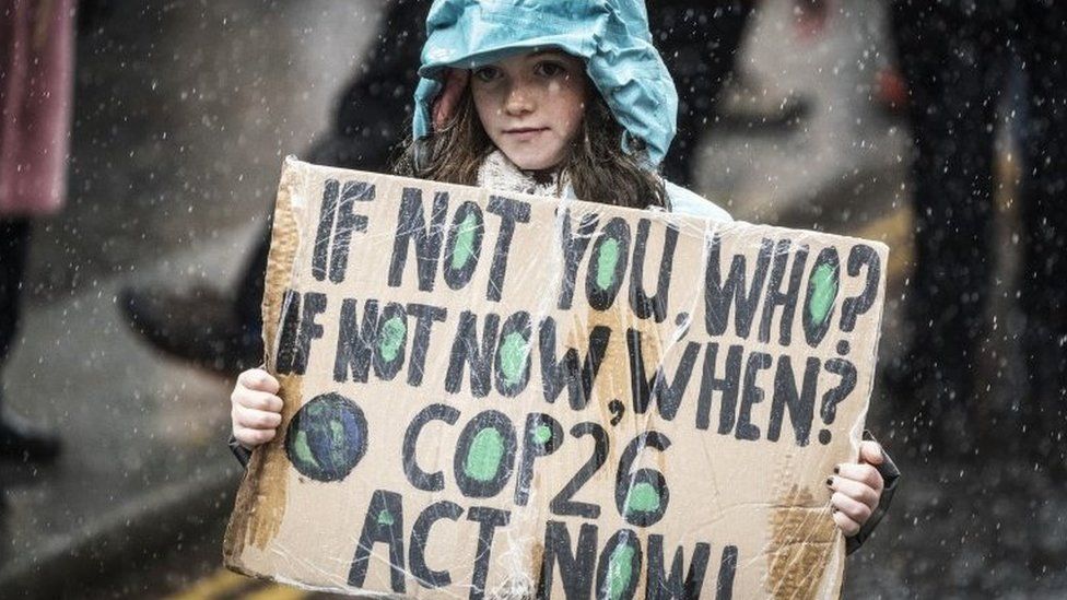 Girl holding a sign saying "If not you, who? If not now, when? COP26 Act Now"