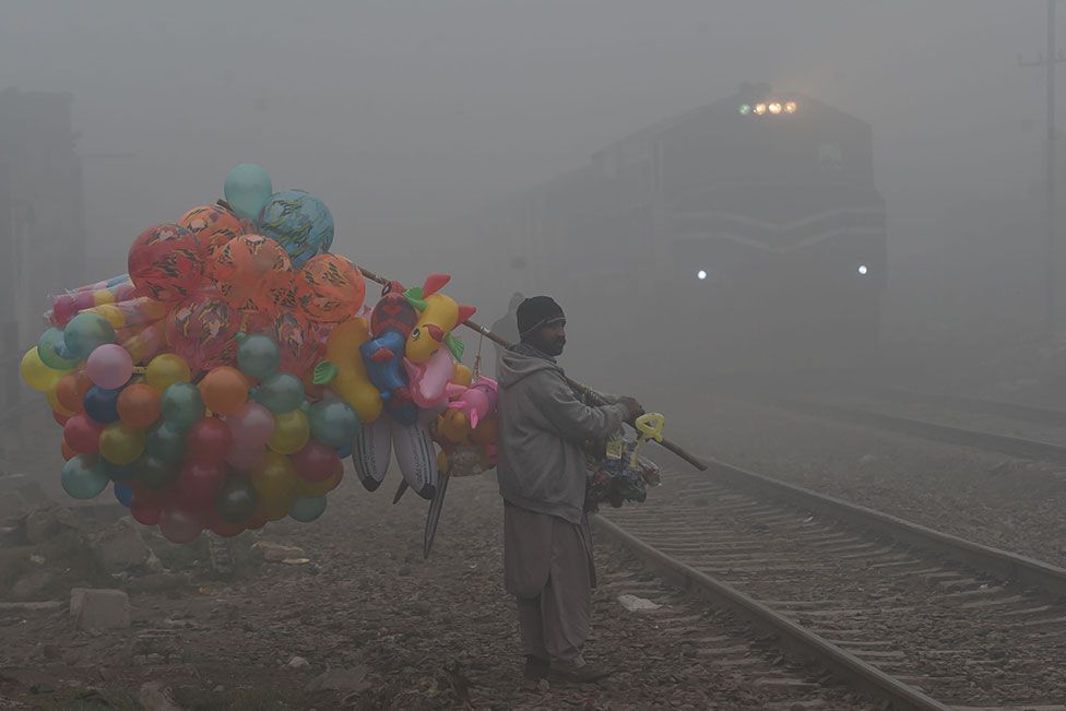 A balloon vendor waits to cross rail tracks amid foggy conditions in Lahore, Pakistan, on 13 January 2022