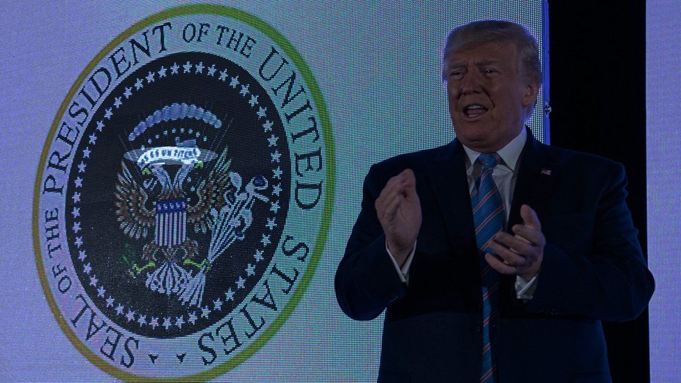 Mr Trump stands beside the doctored seal