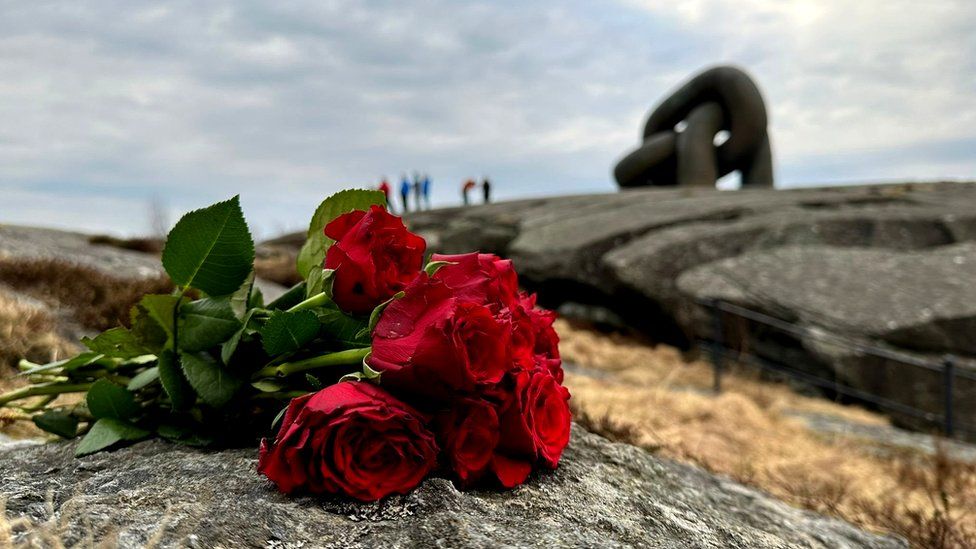 Red roses on a rock beyond which is a large metal sculpture