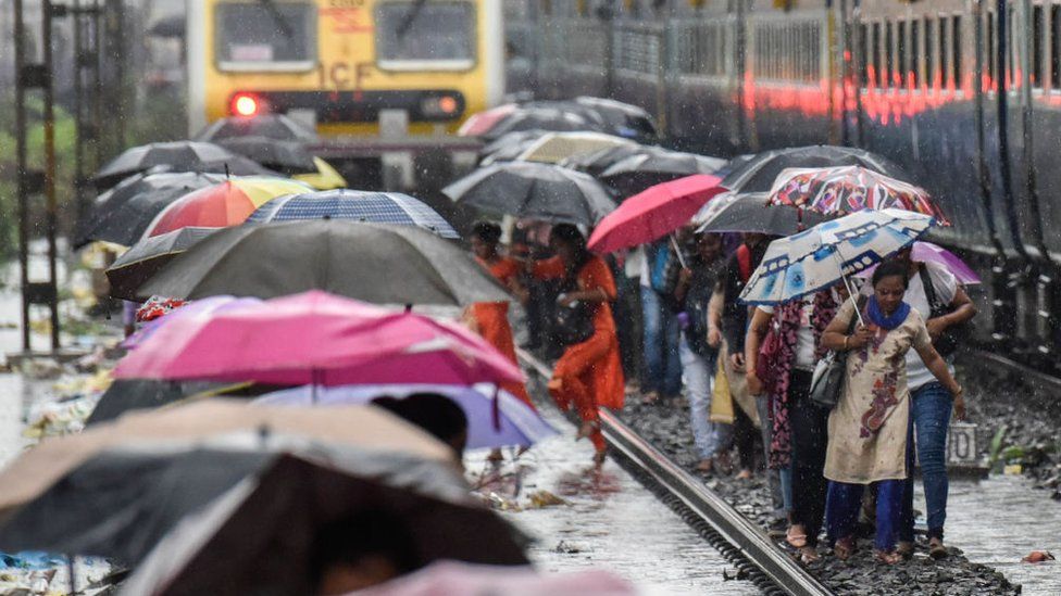 People walk on the railway tracks as heavy monsoon rains hit the local train services near Sion on July 1, 2019 in Mumbai, India.