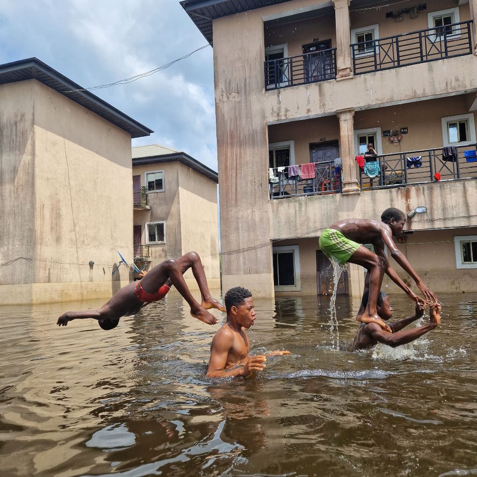 Люди, играющие в паводковых водах возле апартаментов Dorca Executive Apartments (студенческое общежитие) в муниципалитете Огбия, штат Байелса, Нигерия, ноябрь 2022 г.