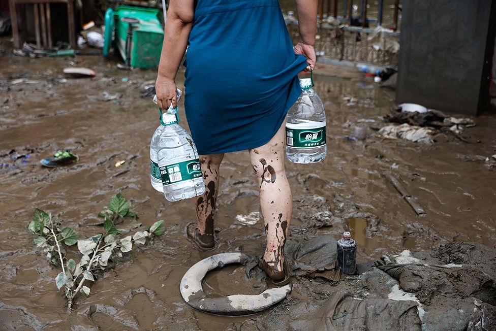 A resident holding bottles of water as she walks back to a residential compound, after remnants of Typhoon Doksuri brought rains and floods in Beijing, China August 2, 2023. REUTERS/Tingshu Wang