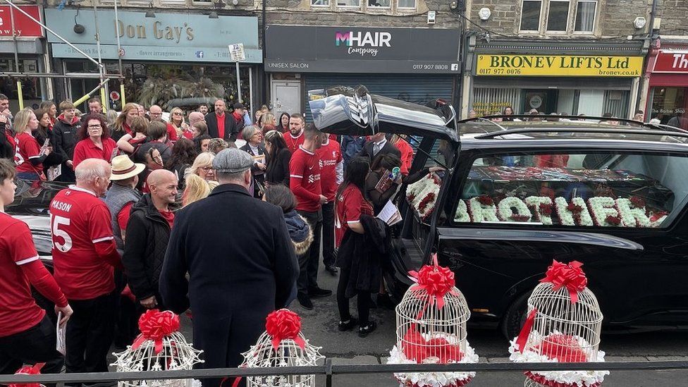 Mourners dressed in red gather around a hearse ahead of the funeral of Mason Rist in Bristol