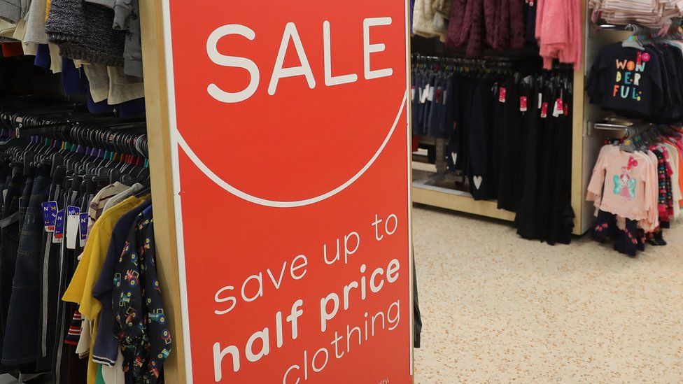 Racks of children's clothes with a big sale sign at one end