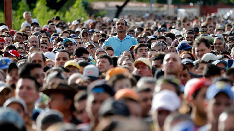 A man peaks over the crowd waiting to cross the border into Colombia from Venezuela on 17 July