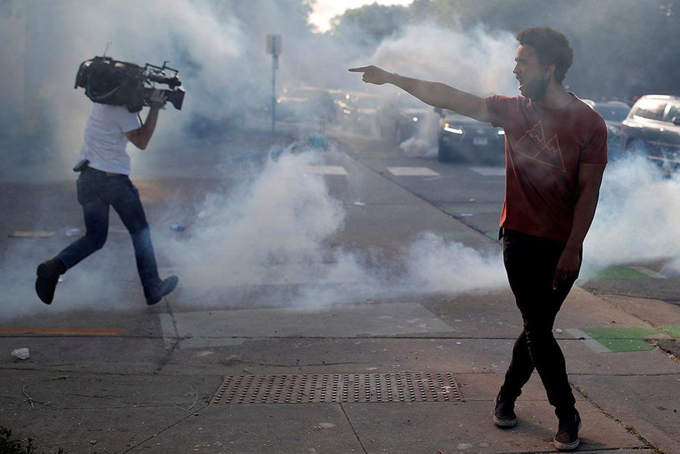 A protester argues with law enforcement officers as a cameraman runs from tear gas during a demonstration in Minneapolis on 31 May