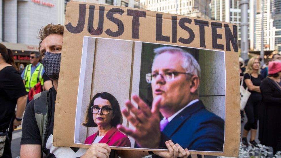 A protester holds up a sign urging Prime Minister Scott Morrison to listen to women's accounts