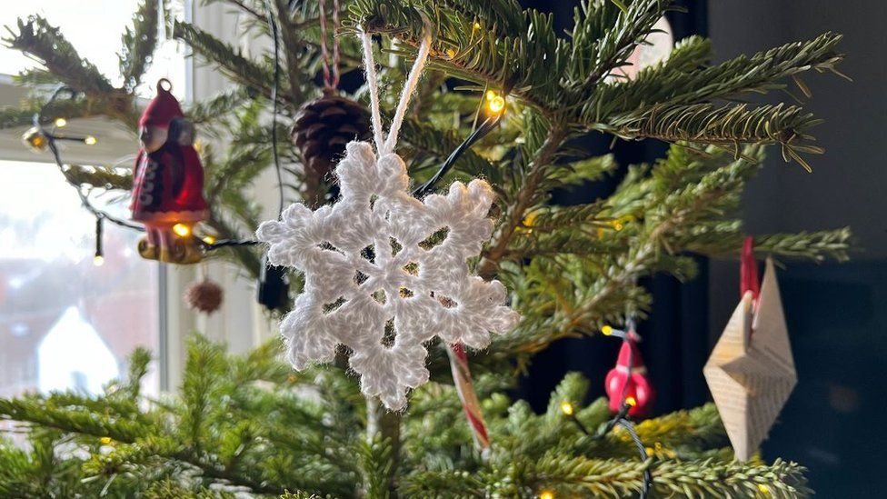 a crocheted snowflake hanging on a christmas tree with other paper and wooden baubles