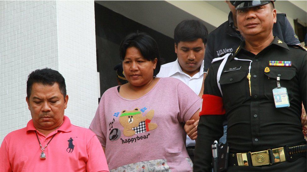 Ms Patnaree Chankij, wearing a pink T-shirt reading 'happybear' being escorted by police down a staircase, as she leaves a military court in Bangkok on 8 May 2016