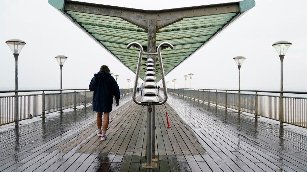A person makes their way through the rain at Boscombe Pier in Dorset