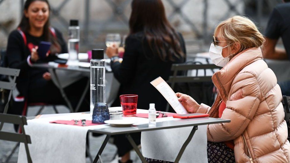 A woman reads a menu as she sits at a restaurant terrace in Rome, on October 25, 2020