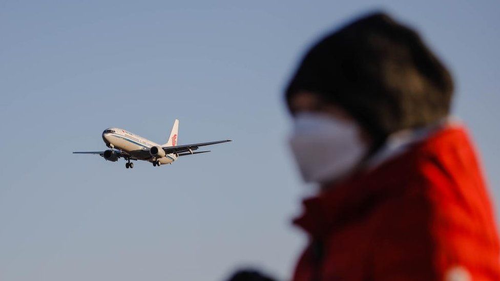 A person is pictured wearing a mask in front of a passenger airplane landing in Beijing, China