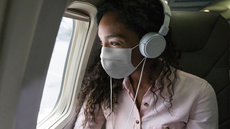 Stock image of a young woman wearing a face mask travelling on a plane