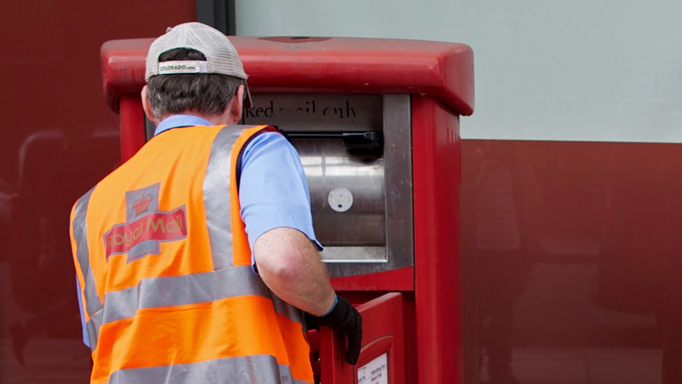 A postman empties a Royal Mail post box