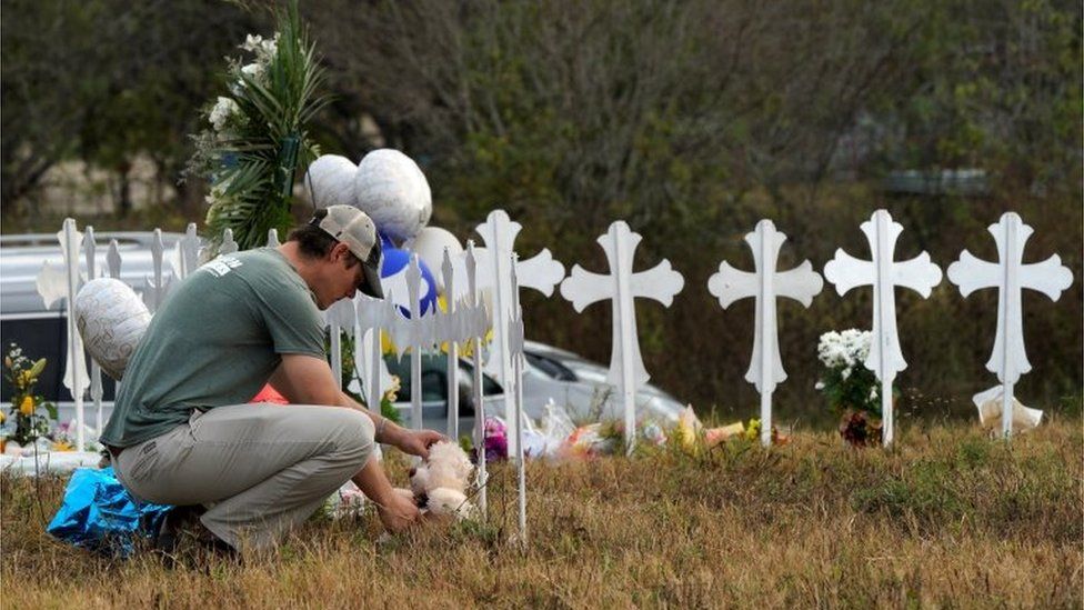 A man places a Teddy bear near a row of memorial crosses in Sutherland Springs, Texas.