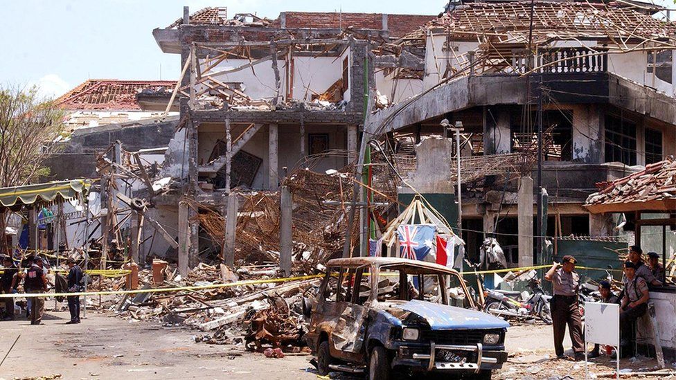 The aftermath of the Bali bombing, showing the damaged building and a burnt-out car.
