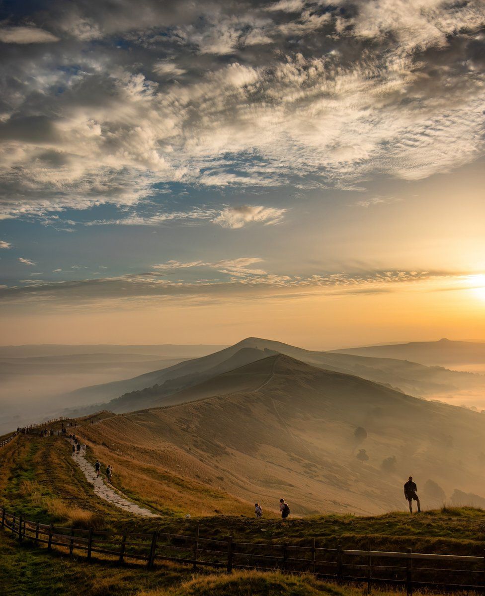 People walking along a hill path at sunset