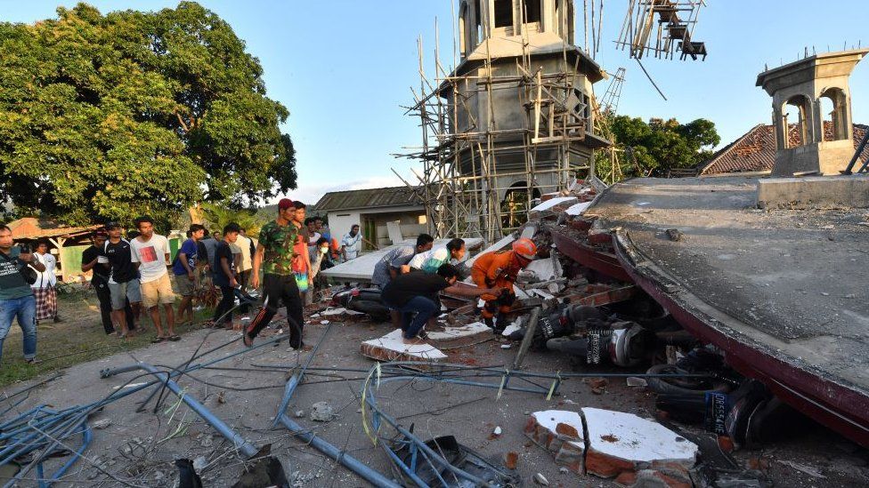 Residents and Indonesian search and rescue personnel look under the ruins of a mosque in Pemenang
