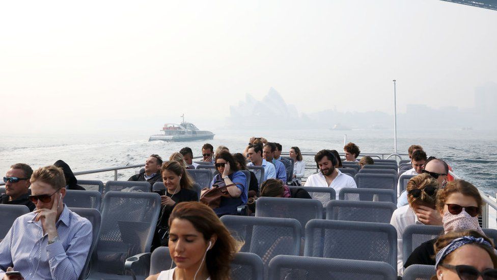 Passengers on a ferry on Sydney Harbour during a smoke haze across the city which has almost obscured the Sydney Opera House in the background