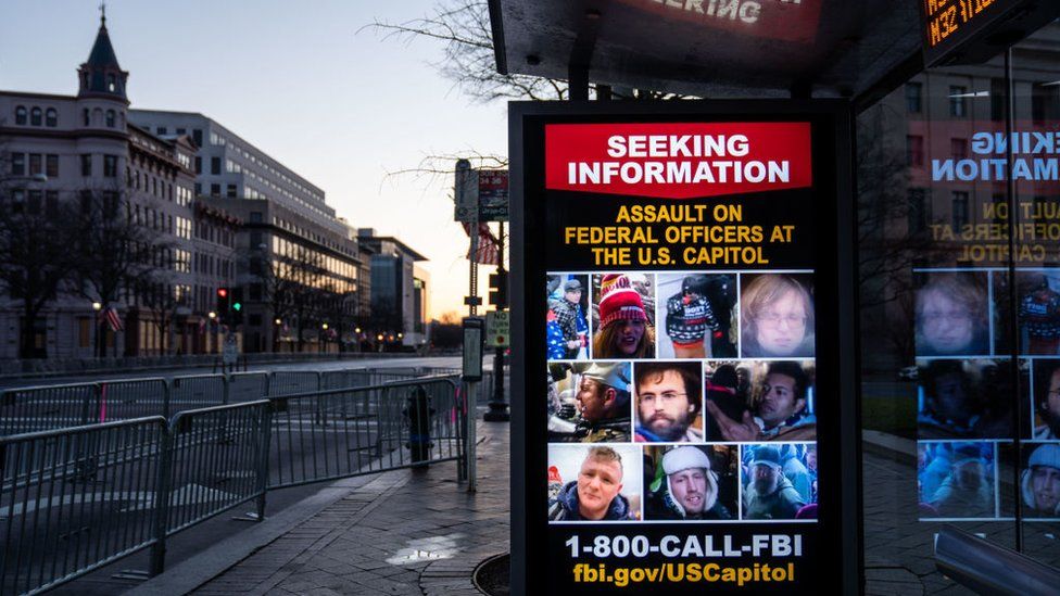Знак, ищущий информацию о людях, которые ворвались в здание Капитолия, виден на восходе солнца с Пенсильванской авеню, которая находится в безопасной зоне вокруг центра Вашингтона в субботу, 16 января 2021 года, в Вашингтоне, округ Колумбия.