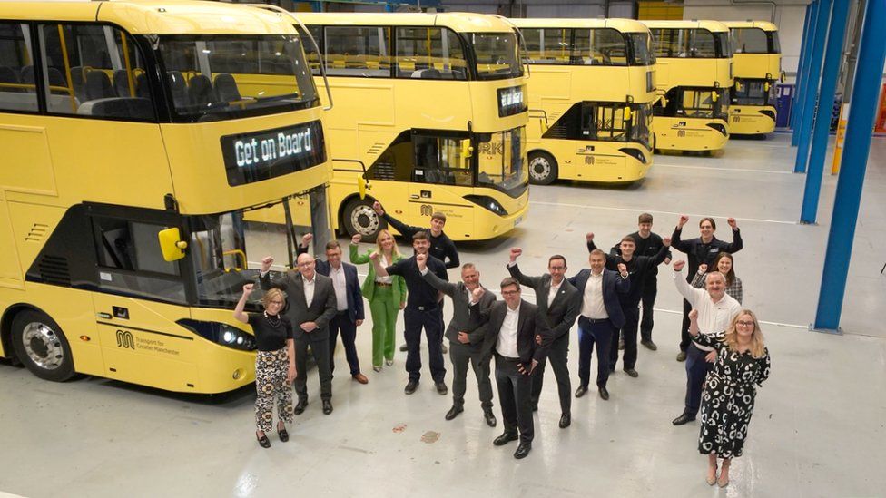 apprentices and bosses form M shape in front of the buses