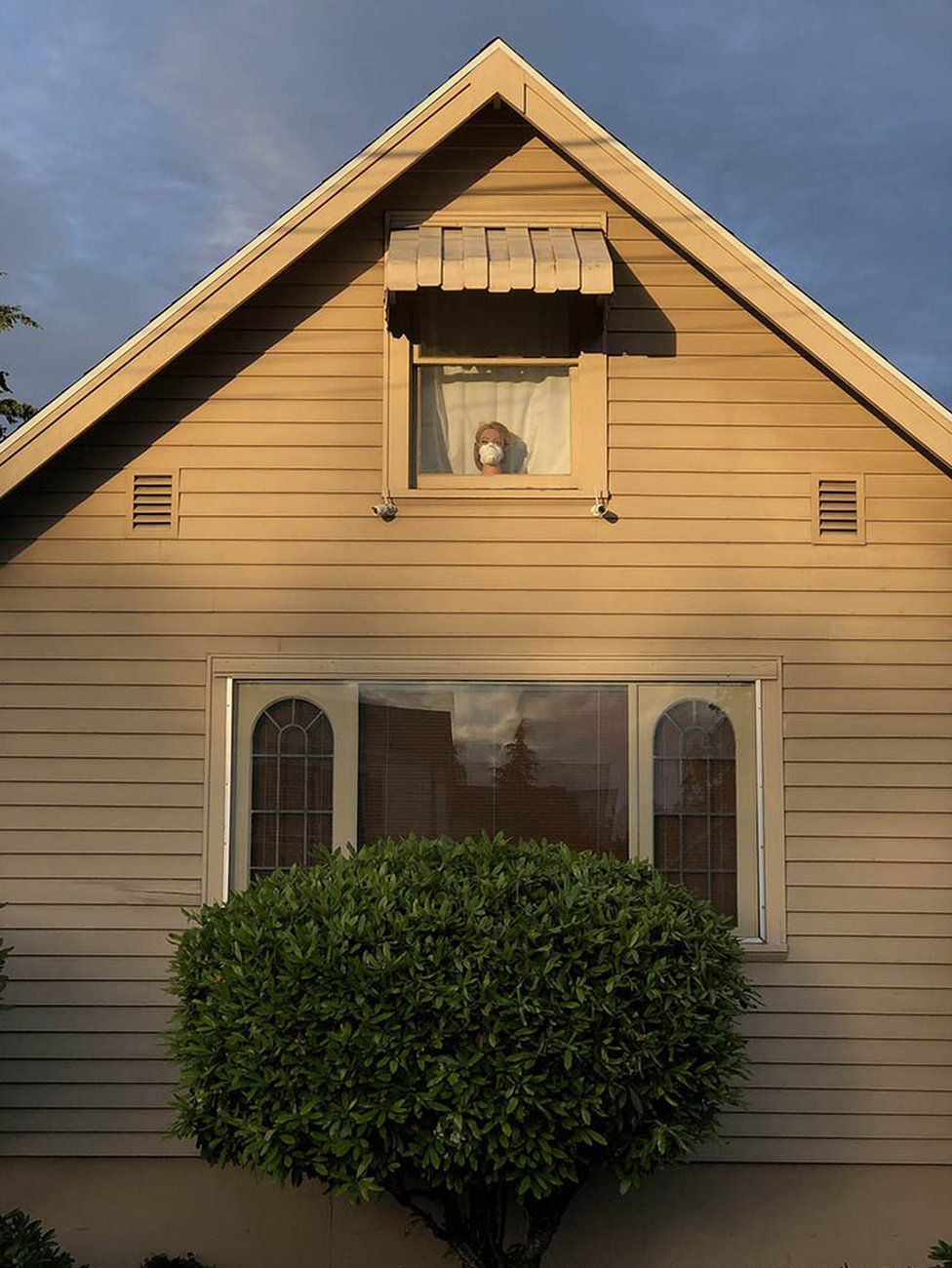 Exterior of a house with a mannequin head wearing a mask visible through a window