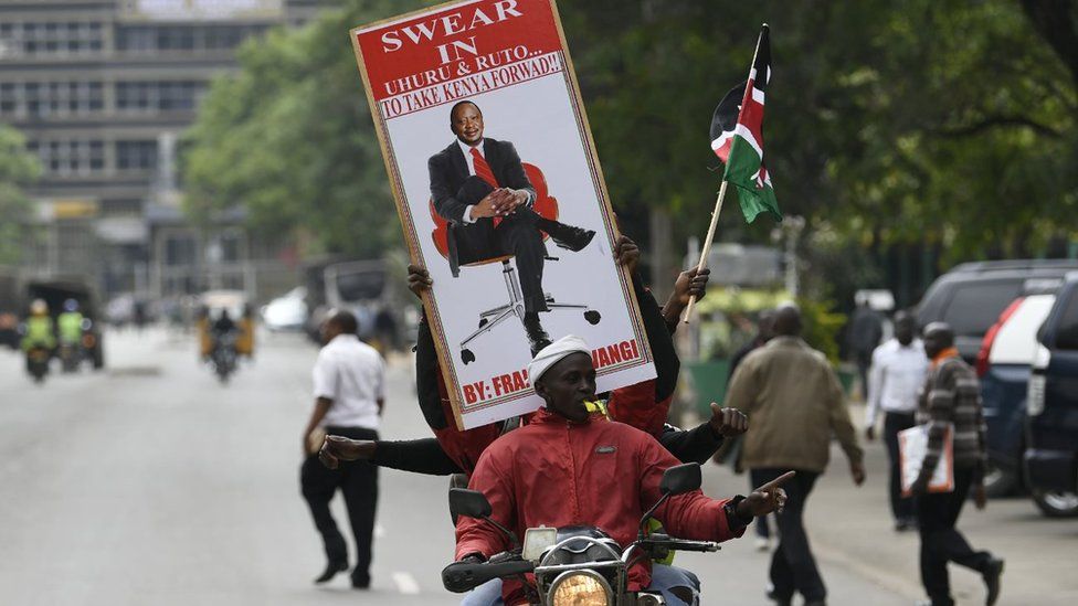 Supporters of President Uhuru Kenyatta hold a banner bearing a picture of Kenyatta as they celebrate on November 20, 2017 in Nairobi after Kenya's Supreme Court dismissed two petitions to overturn the country's October 26 presidential election re-run, validating the poll victory of Kenyatta