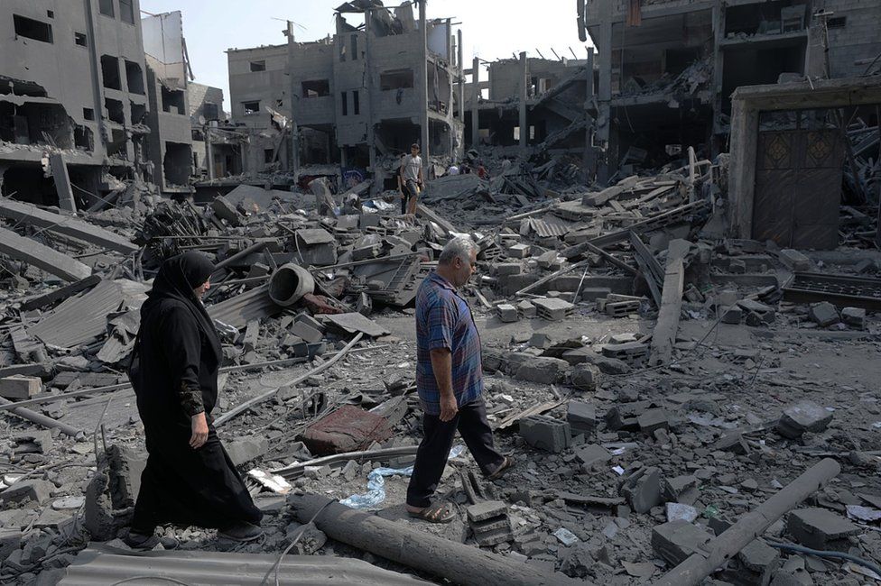 Palestinians walk past buildings destroyed in Israeli air strikes in northern Gaza (28 October 2023)