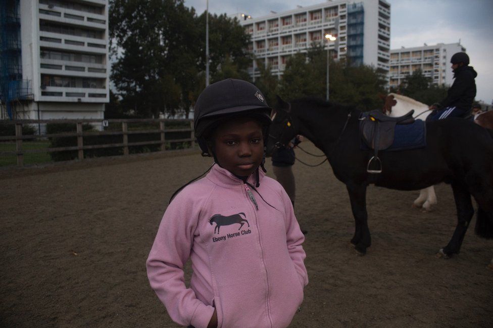 A small girl stands in a riding hat