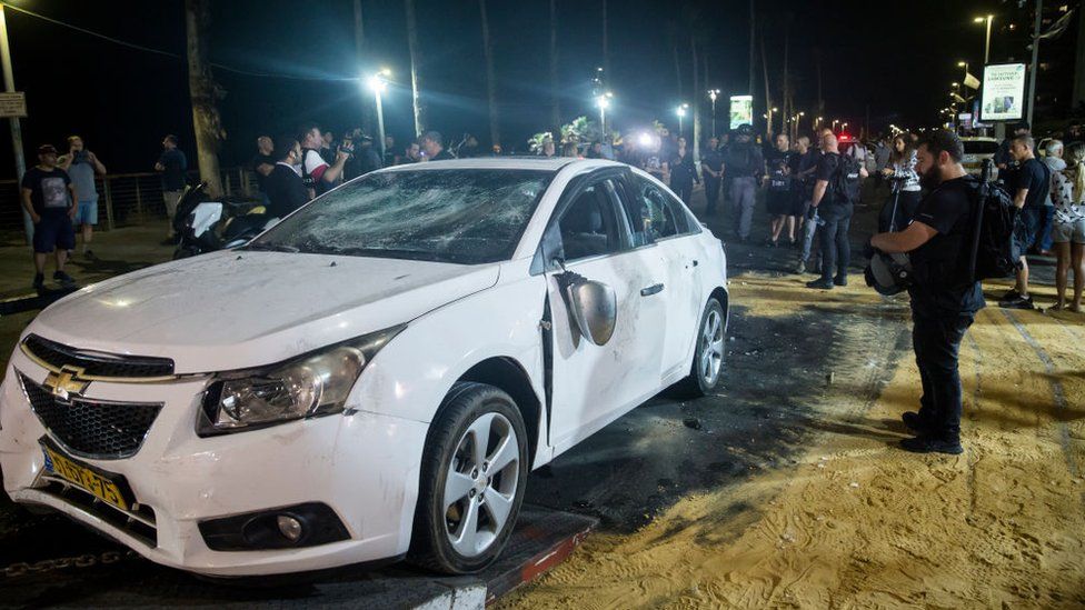 Police inspect damage to a car attacked by a Jewish mob on Wednesday night